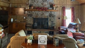 Un intérieur de chalet chaleureux avec une cheminée en pierre, des poutres en bois et un ventilateur de plafond.