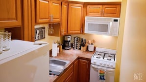 A compact kitchen with wooden cabinets, a microwave, a coffee maker, and a gas stove.