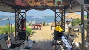 A beach house with a wooden deck, outdoor seating, and a view of the water and a bridge.