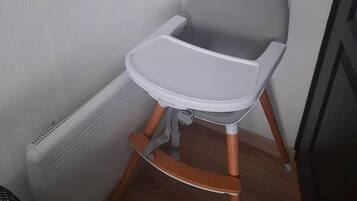 Une pièce d’angle avec un radiateur blanc, un plancher en bois et une chaise haute pour bébé de couleur grise.
