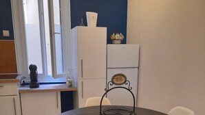 Ein Essbereich mit einem runden Tisch, weißen Stühlen, einer Kaffeemaschine und einem Kühlschrank.