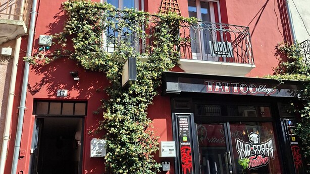 Ein rotes Gebäude mit einer schwarzen Fassade, auf der 'Tattoo Shop' steht, und einem gut sichtbaren Eingang.