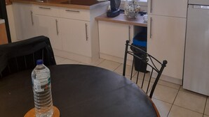 Eine kompakte Küche mit Spüle, Herd und Kühlschrank. Ein Esstisch mit einem Stuhl und einer Wasserflasche stehen bereit.