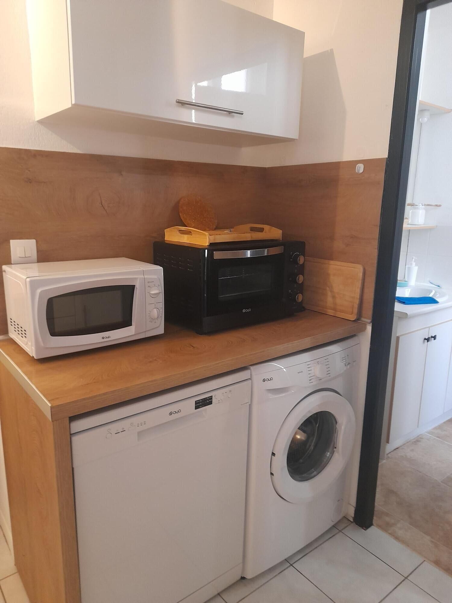 Een compact keukenhoekje met een magnetron, broodrooster en wasmachine.
