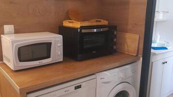 Een compact keukenhoekje met een magnetron, broodrooster en wasmachine.