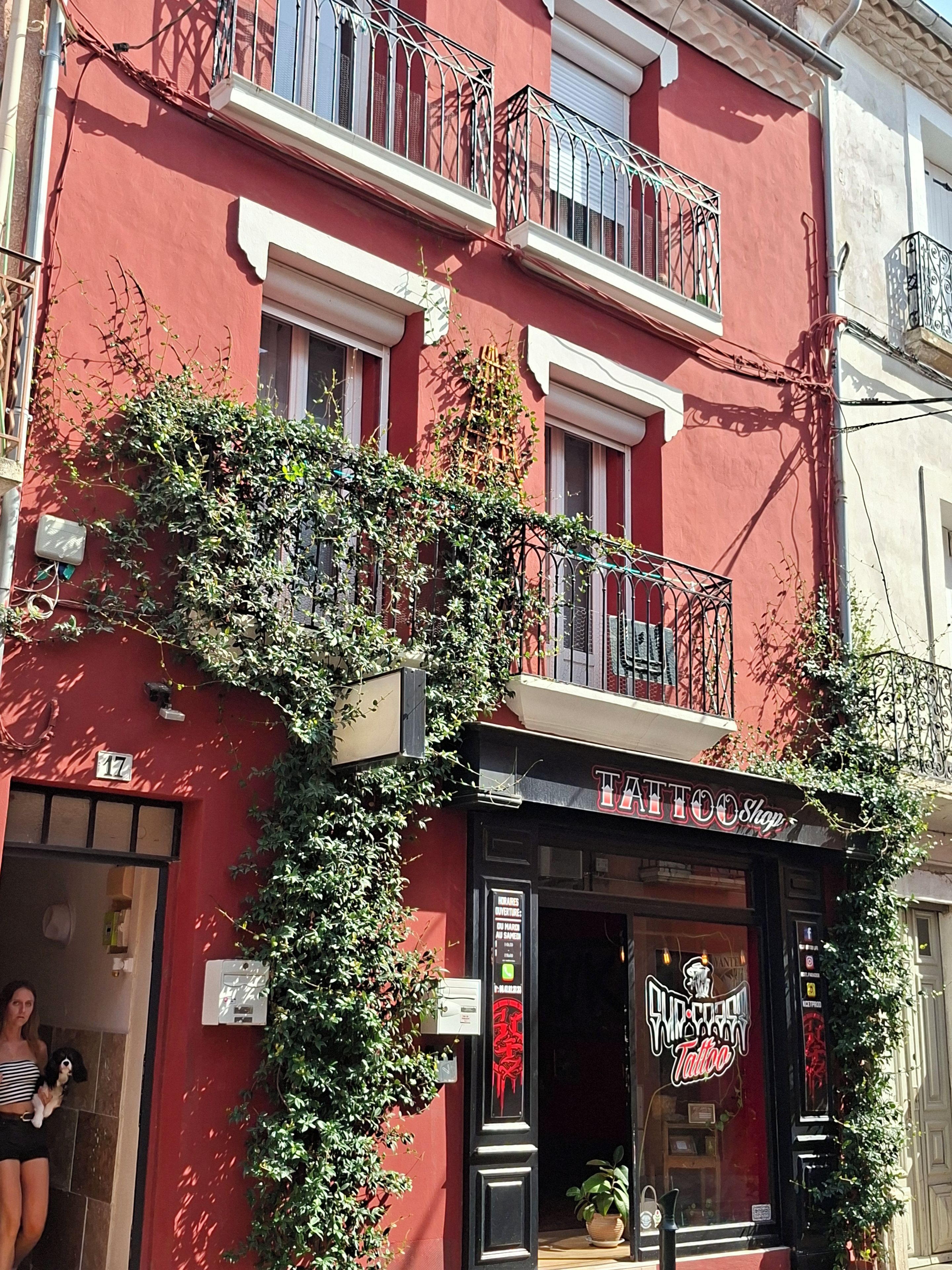 Un bâtiment rouge avec une devanture portant l’inscription « Salon de tatouage » et un balcon doté de rampes en métal.