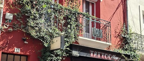 A red building with a storefront labeled 'Tattoo Shop' and a balcony with metal railings.