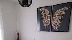 Ein ordentlich bezogenes Bett mit einer weißen und gelben Tagesdecke, zwei schwarze Handtücher und eine hohe Vase mit einer Pflanze.