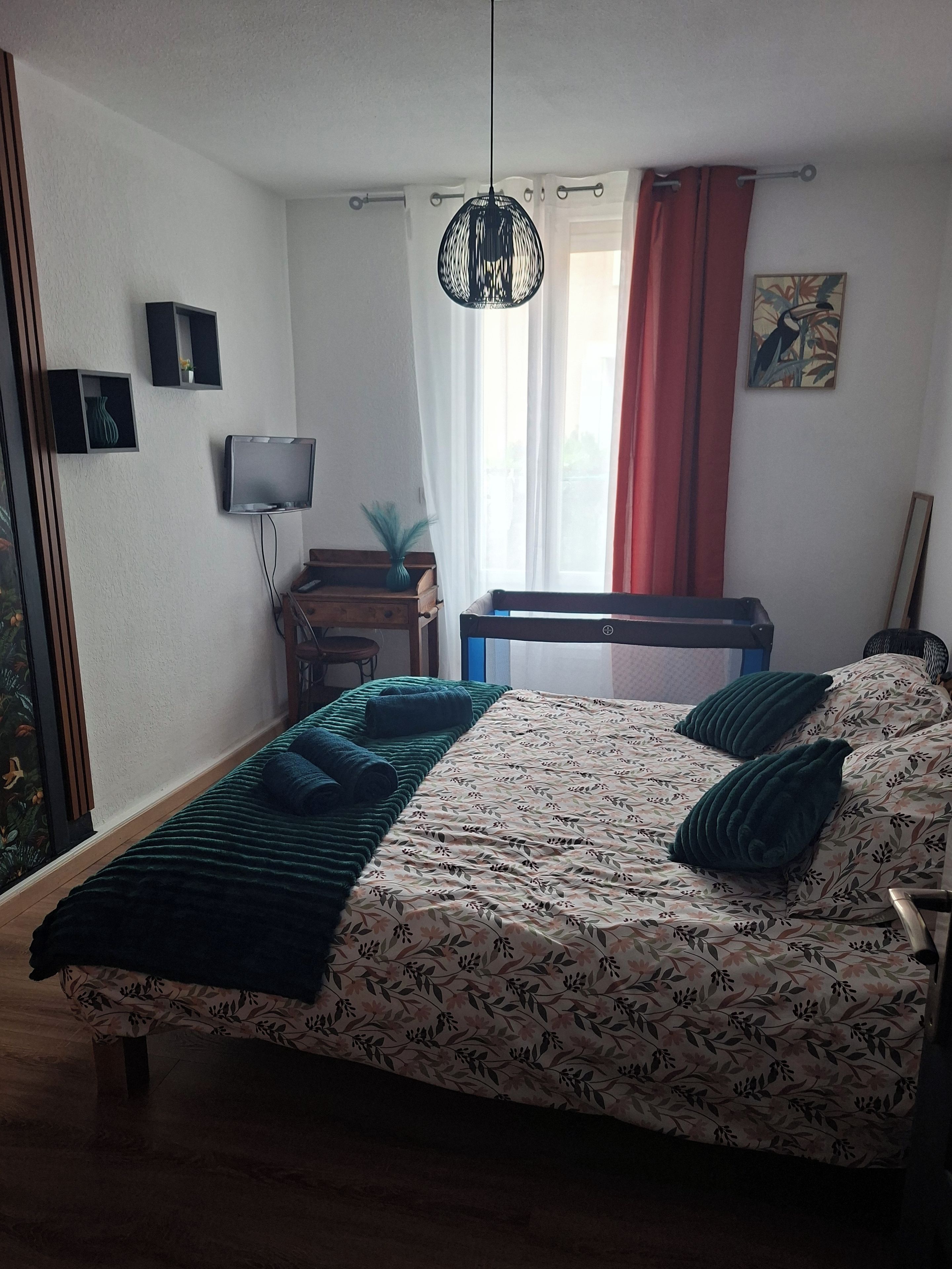 A bedroom with a bed, a TV, a desk, and a window with curtains.
