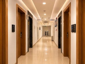Un couloir d’hôtel avec des portes en bois, des panneaux indiquant le numéro des chambres et un sol carrelé propre.