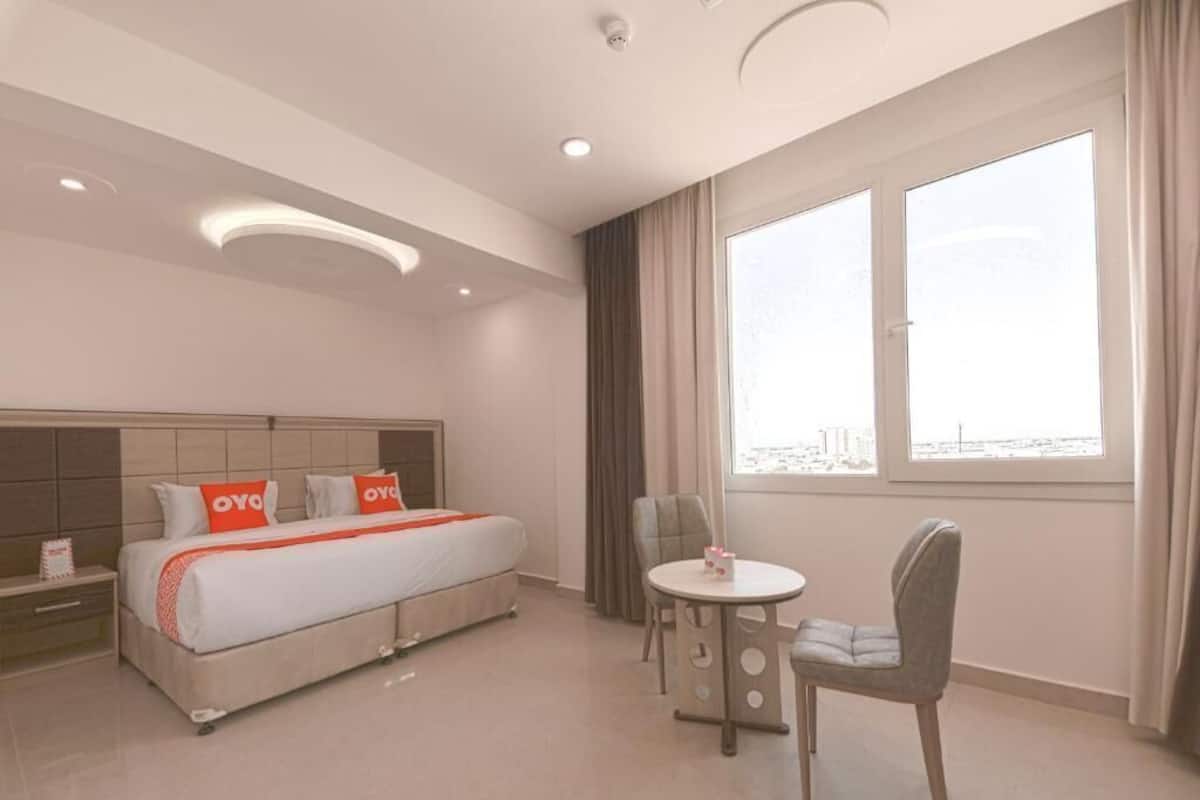 A hotel room with a bed, a chair, a small table, and a window with curtains.