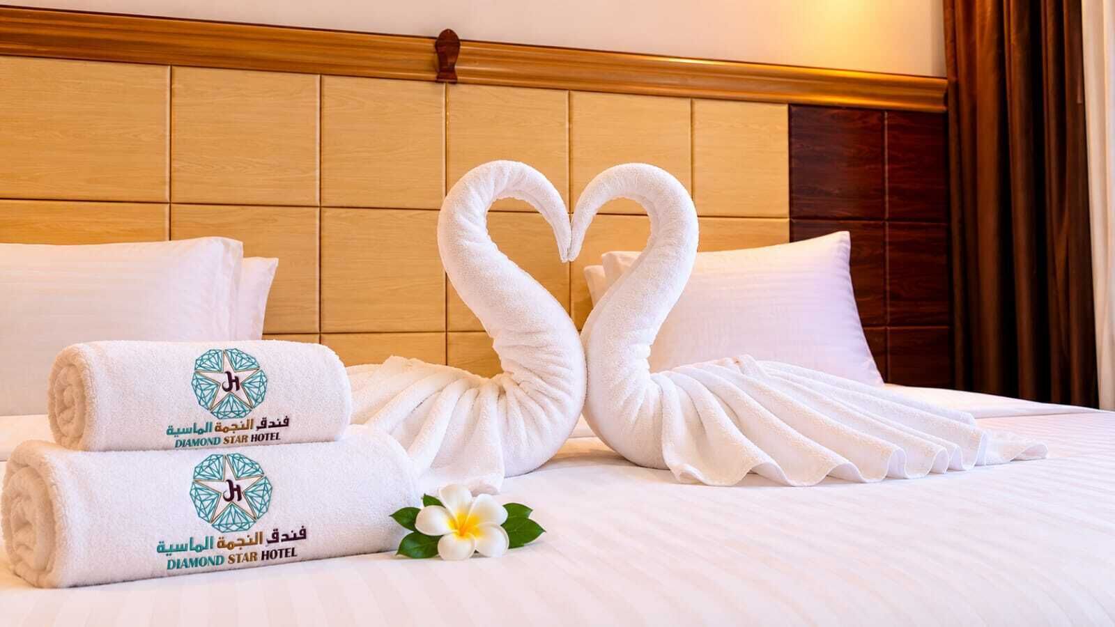 Une chambre d’hôtel avec un lit parfaitement fait, deux serviettes ornées du logo de l’hôtel et deux autres serviettes en forme de cygnes.