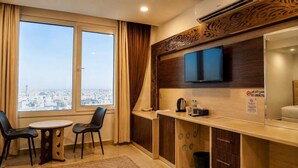 Habitación de hotel con vista a la ciudad, un televisor, una pequeña mesa con sillas, un minibar y un letrero de 'No Fumar'.