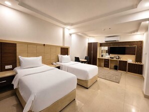 A hotel room with two beds, a desk, a TV, and a wardrobe. - Diamond Star Hotel (Seeb)