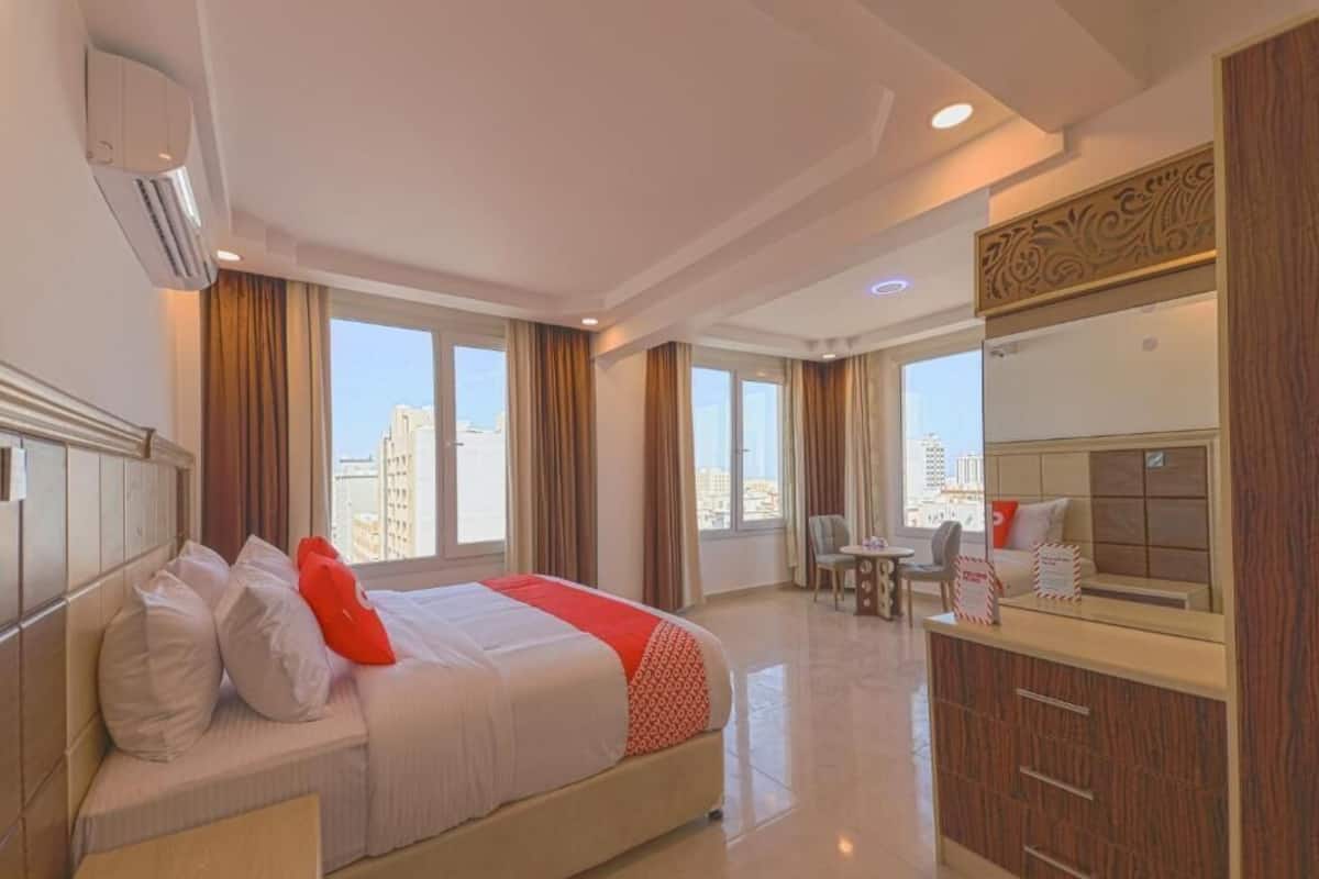 A hotel room with a bed, a desk, a chair, a window with a city view, and an air conditioning unit.