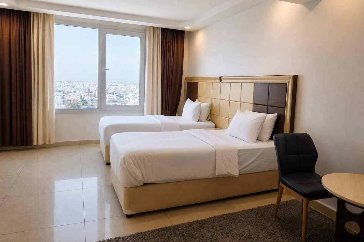 A hotel room with two beds, a view of the city, and a small table.