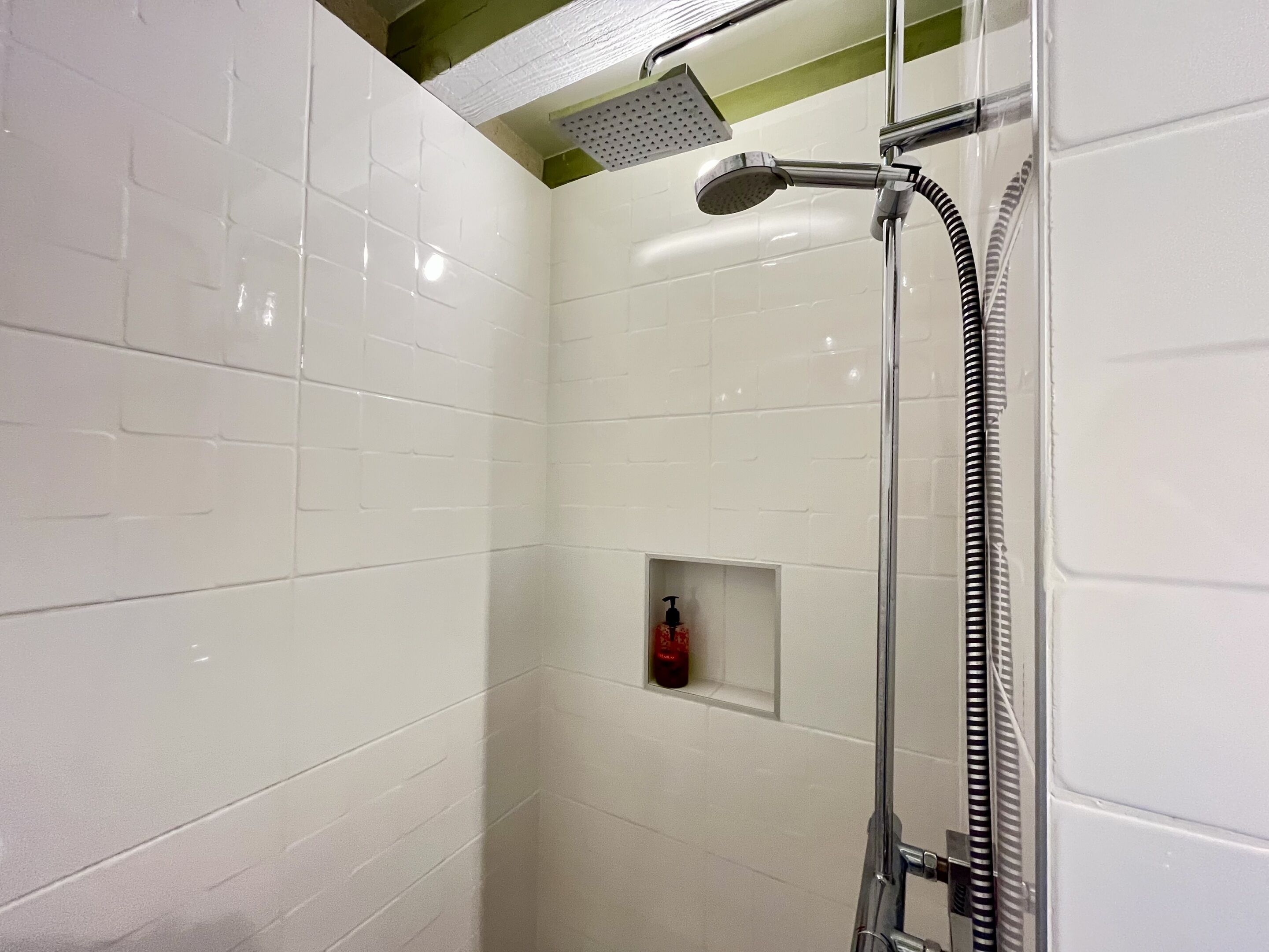Une douche moderne dotée d’un pommeau de douche à main et d’un pommeau de douche à pluie fixé au mur.