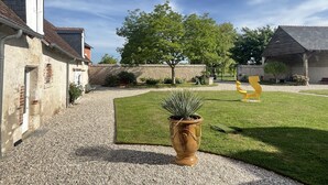 A courtyard with a gravel path, a large potted plant, a yellow sculpture, and a stone wall. - Le Clos des Châteaux (Chitenay)