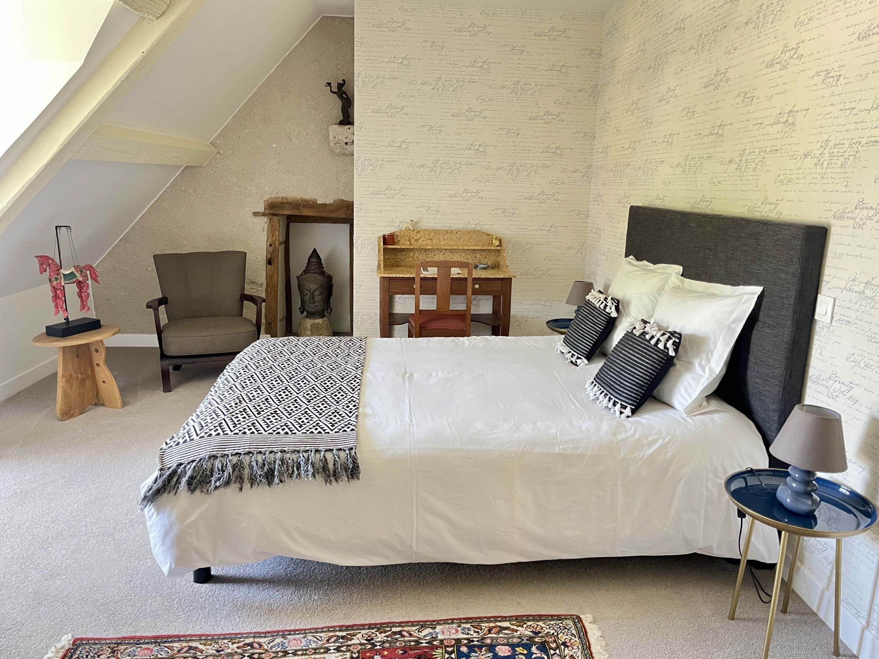 A bedroom with a bed, a chair, a desk, and a small statue.