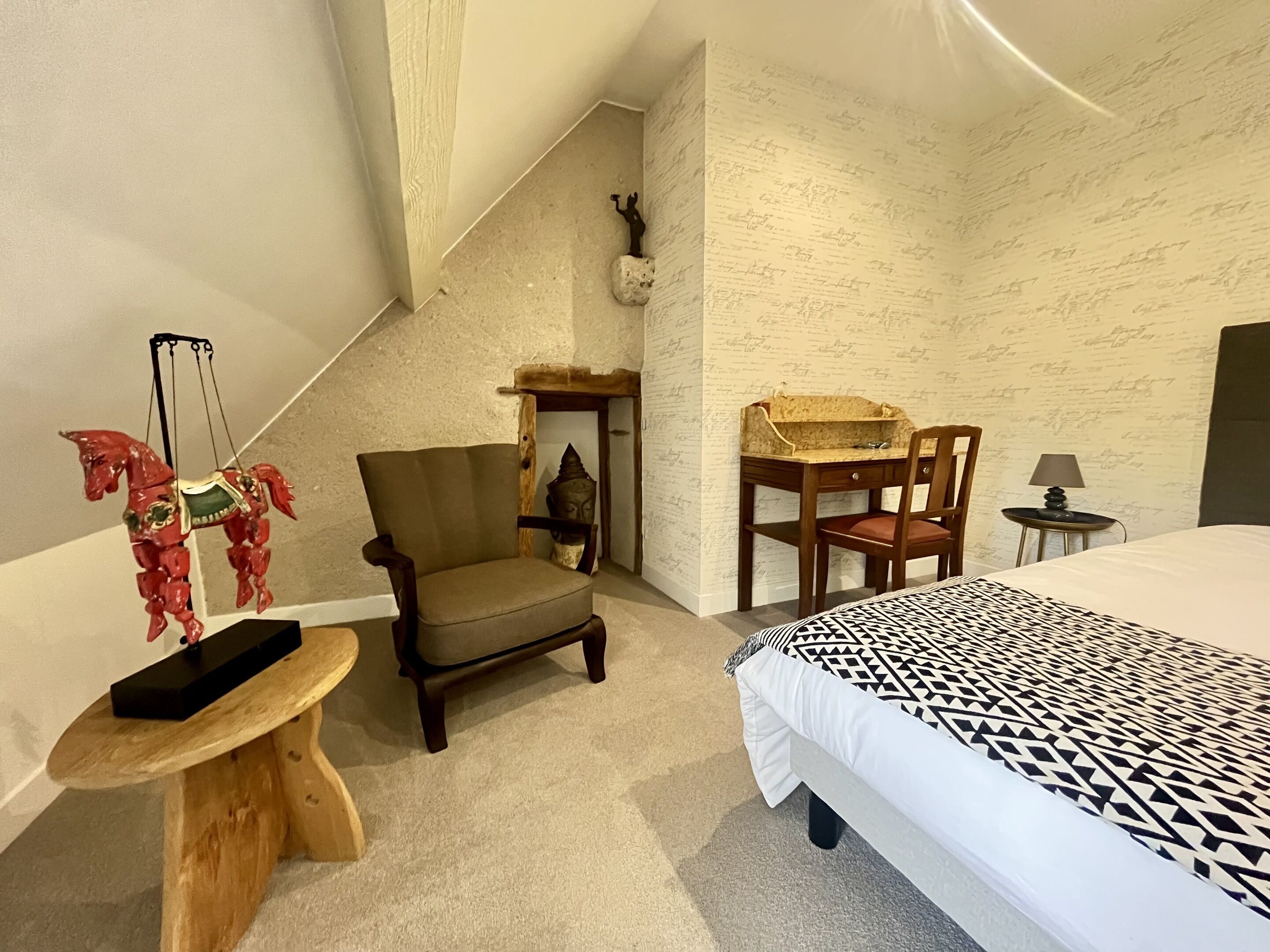 A bedroom with a bed, two chairs, a small table, a decorative horse sculpture, a small statue, and a wall with a textured pattern.