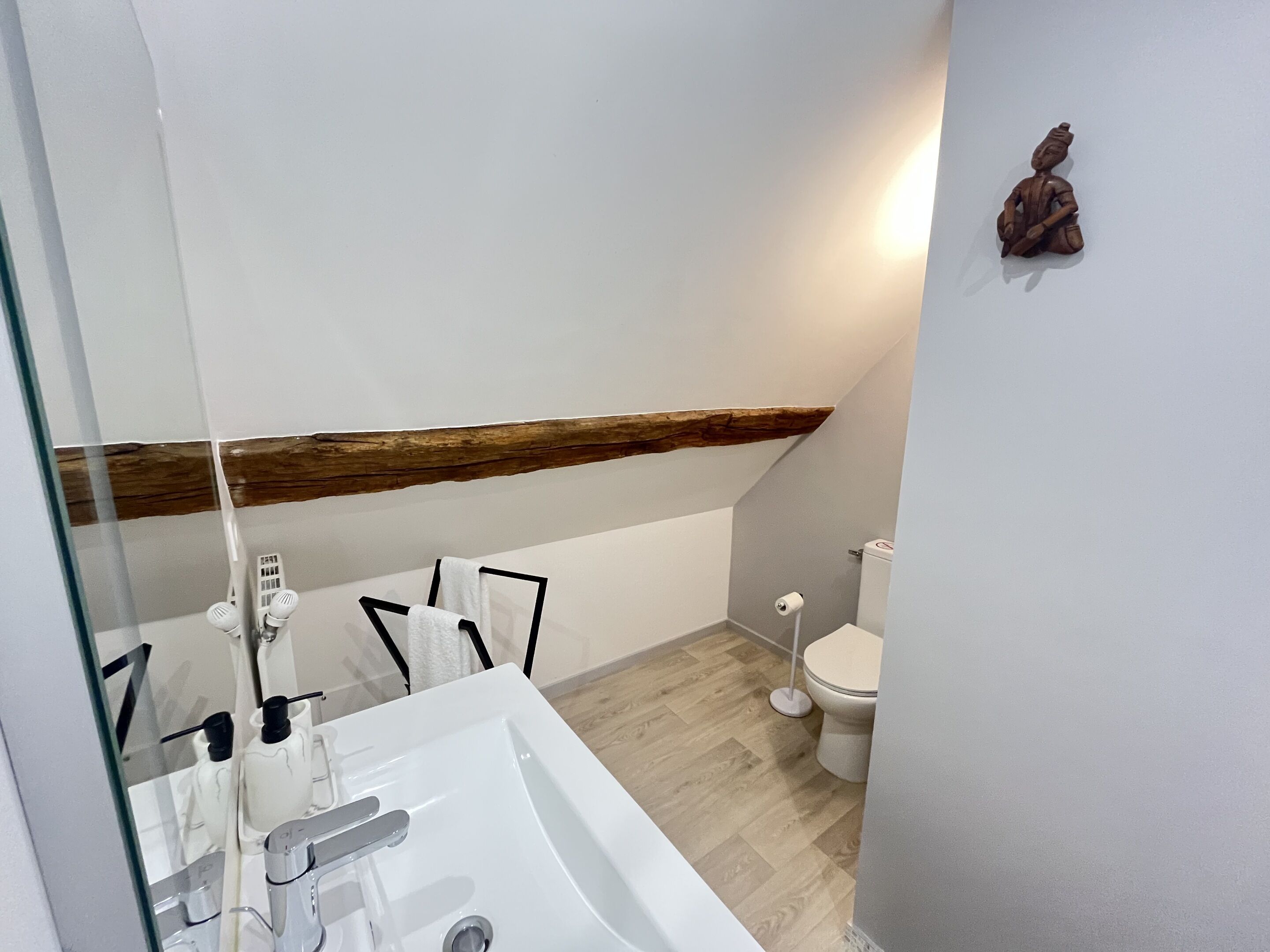 Un baño moderno con un lavamanos blanco, un espejo y un techo con vigas de madera.