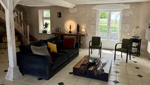 A rustic living room with a dark blue sofa, a wooden coffee table, and a staircase leading to another level. - Le Clos des Châteaux (Chitenay)
