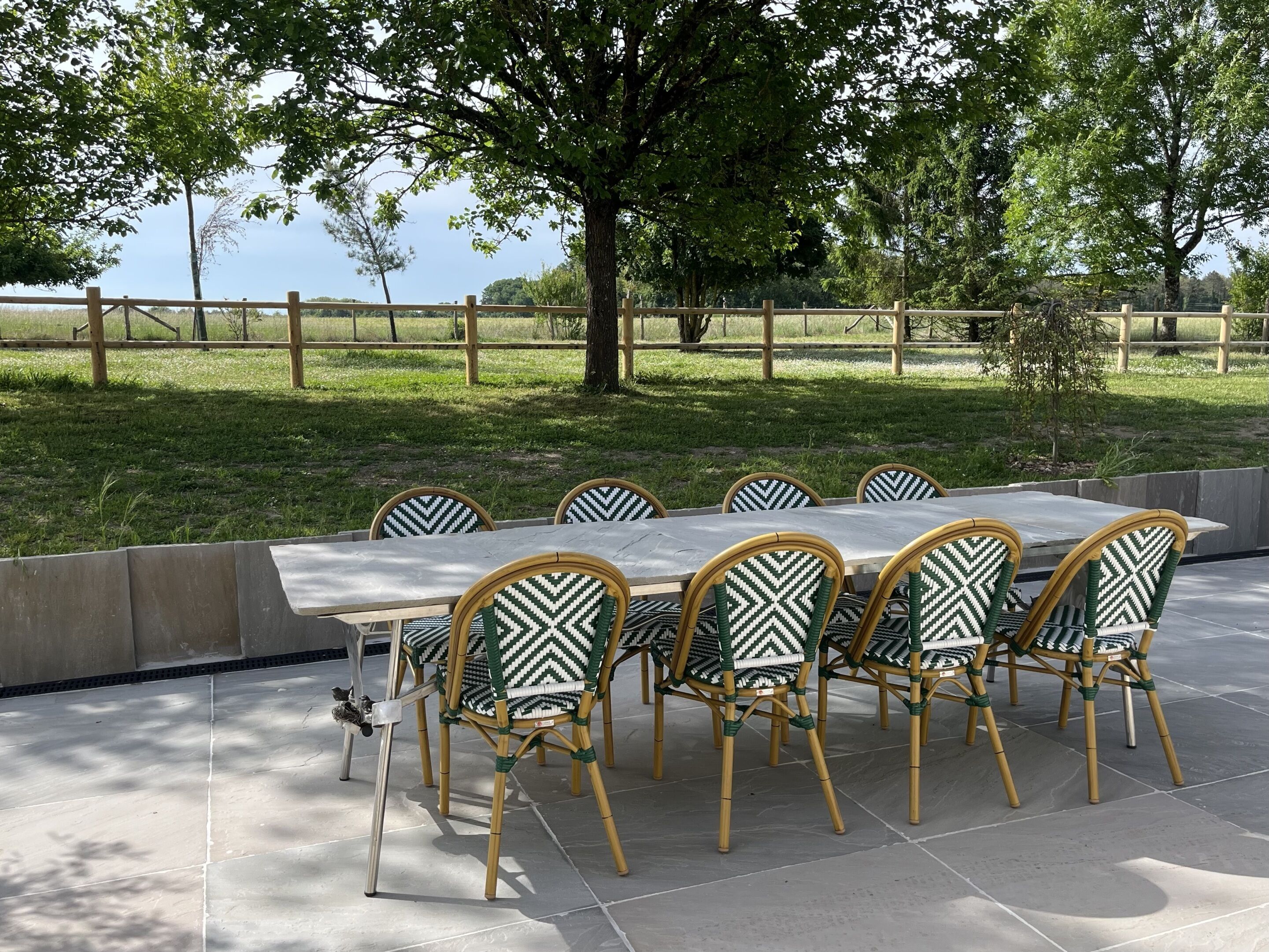 Een buiten eethoek met een lange tafel en zes stoelen, omringd door een houten hek en bomen.