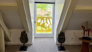 A room with a sloped ceiling, a white door with a golden angel decoration, and two sculptures on the floor. - Le Clos des Châteaux (Chitenay)