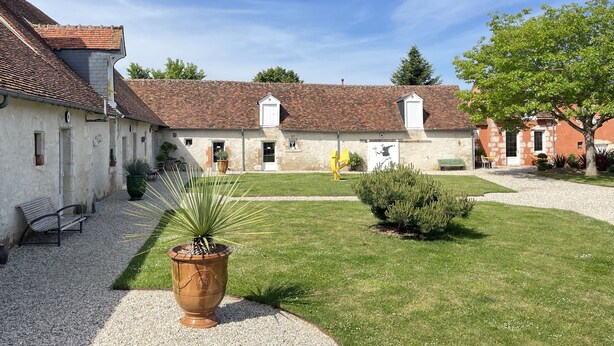 A courtyard with a gravel path, a large planter, and a building with a tiled roof. - Le Clos des Châteaux (Chitenay)
