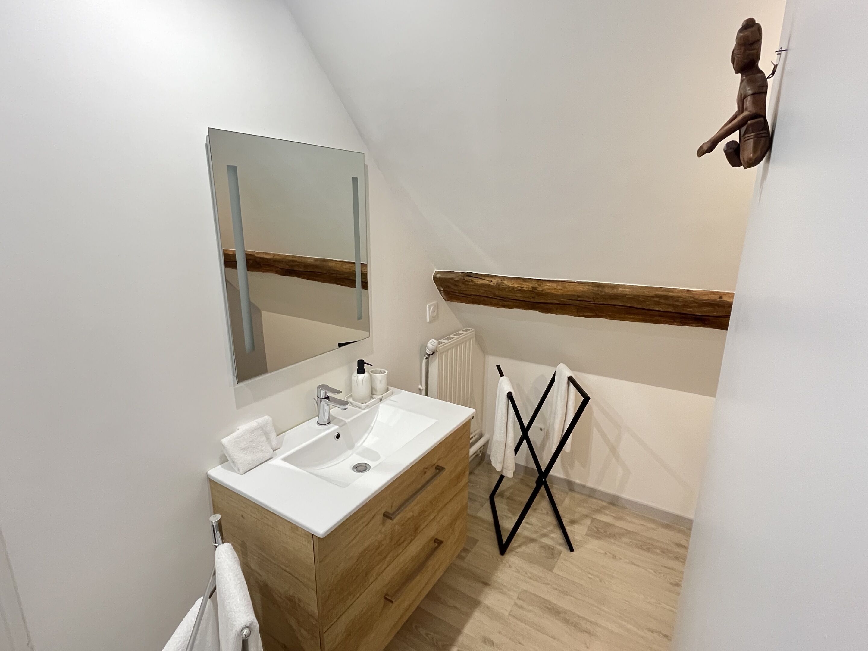 A modern bathroom with a wooden vanity, a large mirror, and a towel rack.