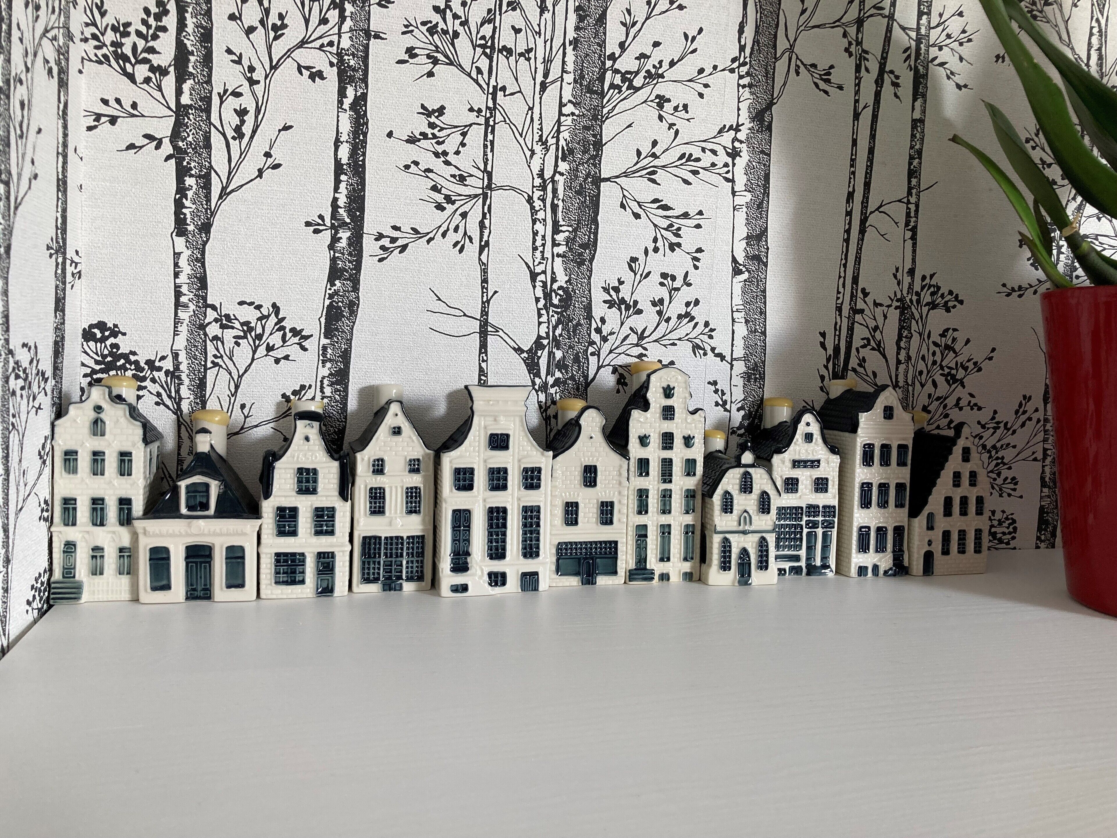 Una hilera de casas en miniatura con techos negros y paredes blancas, con un fondo de diseño arbóreo.