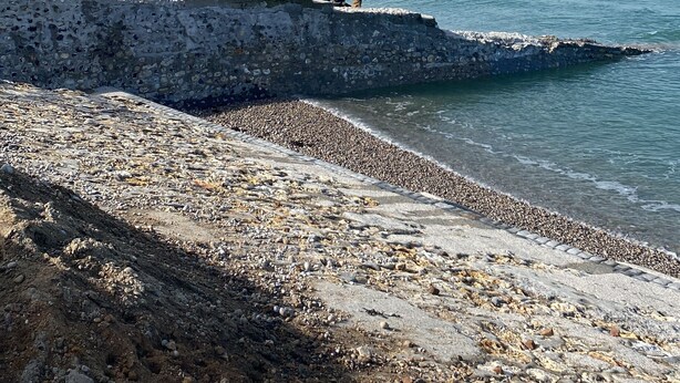 Ein felsiger Strand mit einer großen Felsformation und Blick auf das Meer.