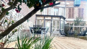 Eine Holzterrasse mit Stühlen, einer Glaseinfriedung und einer Backsteinmauer im Hintergrund.