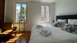 Ein Schlafzimmer mit einem Bett, zwei Fenstern, einem Sessel und einem kleinen Tisch.