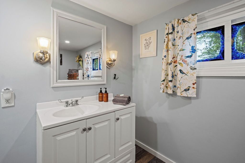 Un bagno con doppio lavabo, un ampio specchio, applique a parete e una finestra con tenda floreale.