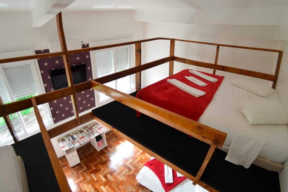 Ein Schlafraum mit Etagenbetten, einer roten Decke, weißen Kissen, einem Holz-Kopfteil und einem kleinen Schreibtisch mit Stuhl.