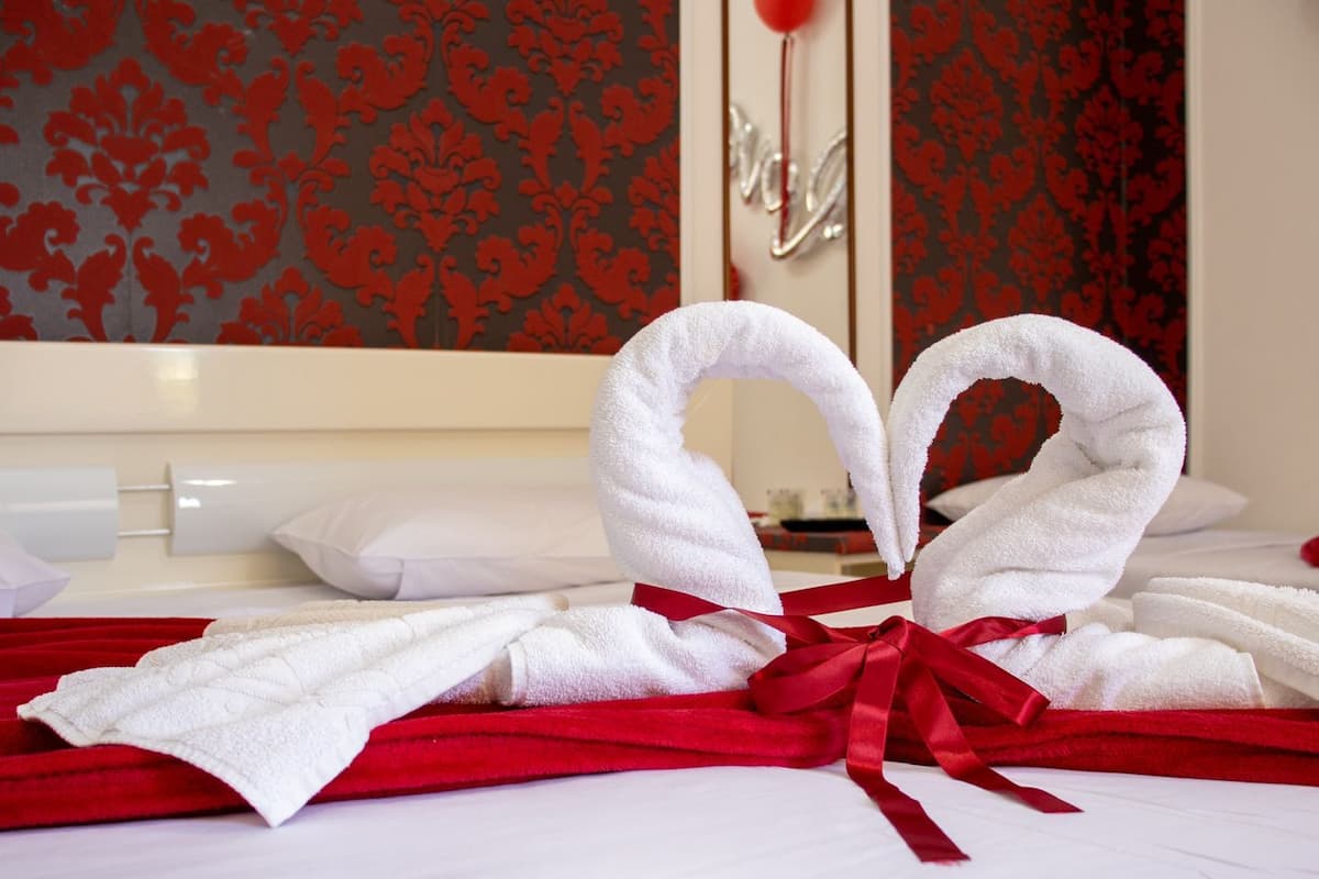 Ein ordentlich gemachtes Bett mit weißen Handtüchern und einer roten Schleife, vor einer Wand mit roten und schwarzen Mustern.