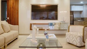 A modern living room with a glass coffee table, a sofa, and a patterned armchair. A large flat-screen TV is mounted on the wall above a wooden panel. - Hermosas piscinas, solo a 5 minutos del mar y salida directa a centro comercial. (Bello Horizonte, Santa Marta)