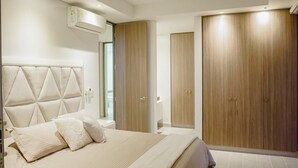 A bedroom with a large bed, a headboard, a wardrobe, and a bathroom visible through an open door. - Hermosas piscinas, solo a 5 minutos del mar y salida directa a centro comercial. (Bello Horizonte, Santa Marta)