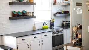 A modern kitchen with white cabinets, a black countertop, and a stainless steel oven. There are shelves with decorative items and a hanging wine rack. - Cozy Cottage perfect for a couple or small family (Durango)