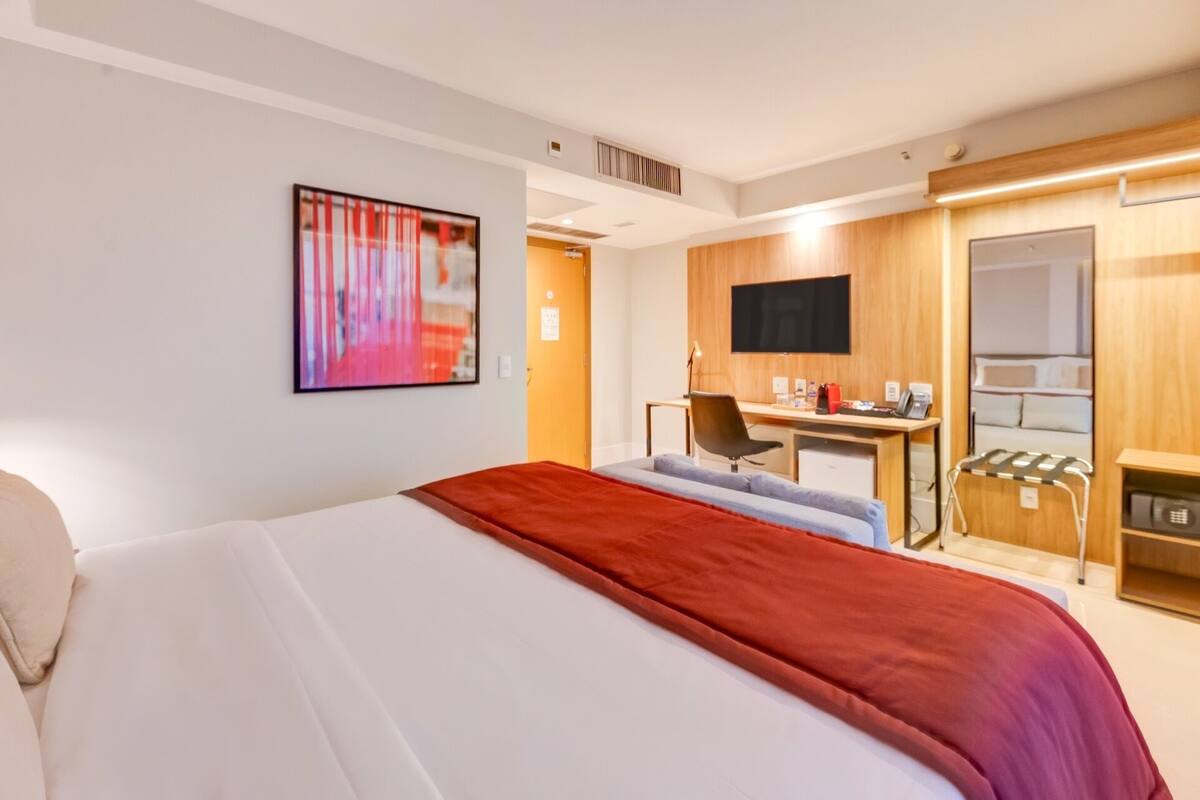 Una habitación de hotel con cama, escritorio, silla, televisor y minibar.
