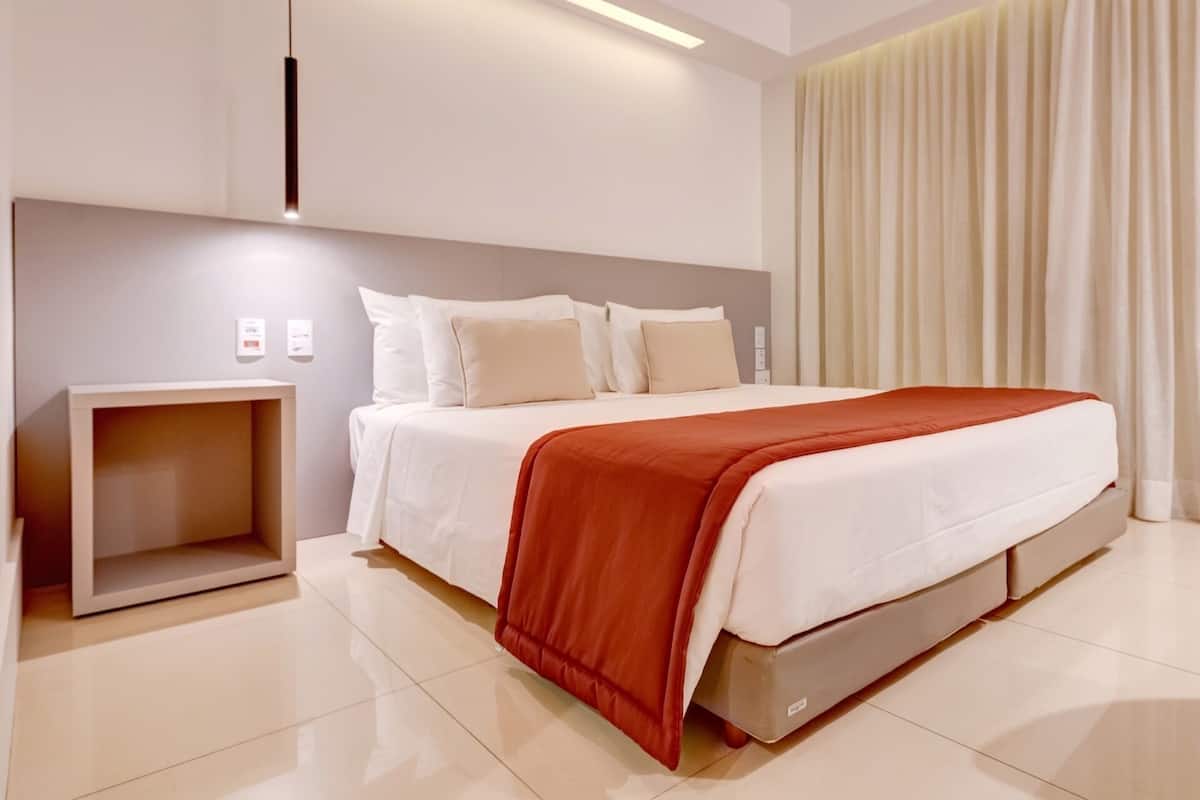 Una habitación de hotel moderna con una cama grande, una mesita de noche y un mueble de almacenamiento integrado.