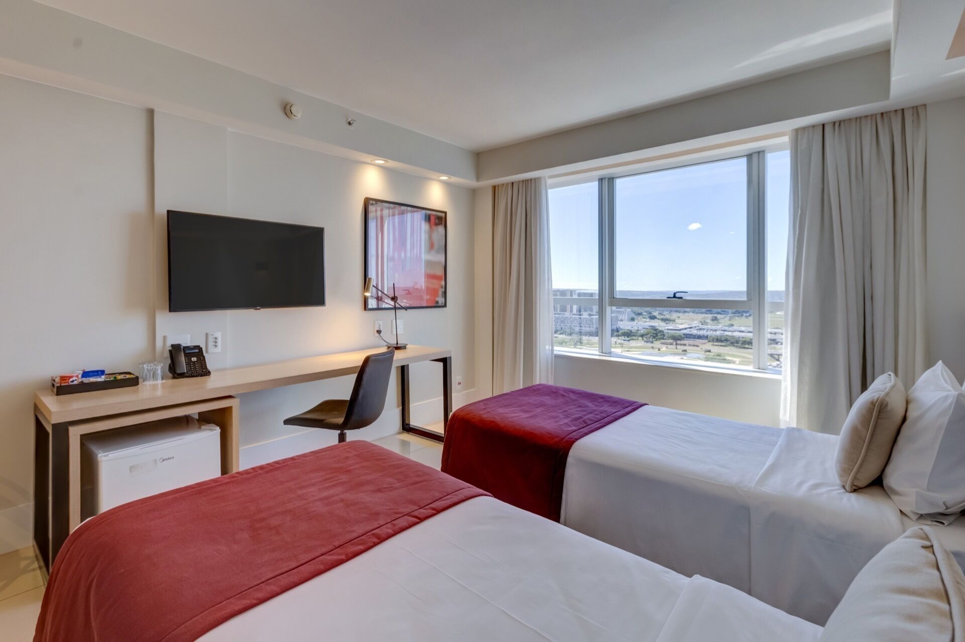 Habitación de hotel con dos camas, un escritorio, un televisor y un ventanal con vistas.