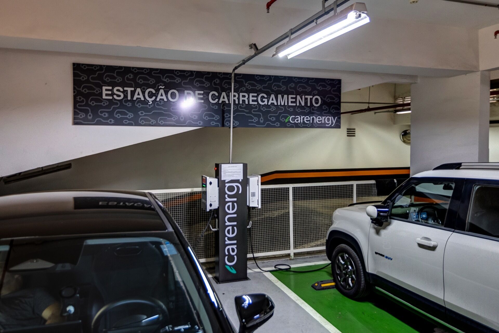 A car charging station with a sign reading 'ESTAÇÃO DE CARREGAMENTO' and 'carenergy' in a parking garage.