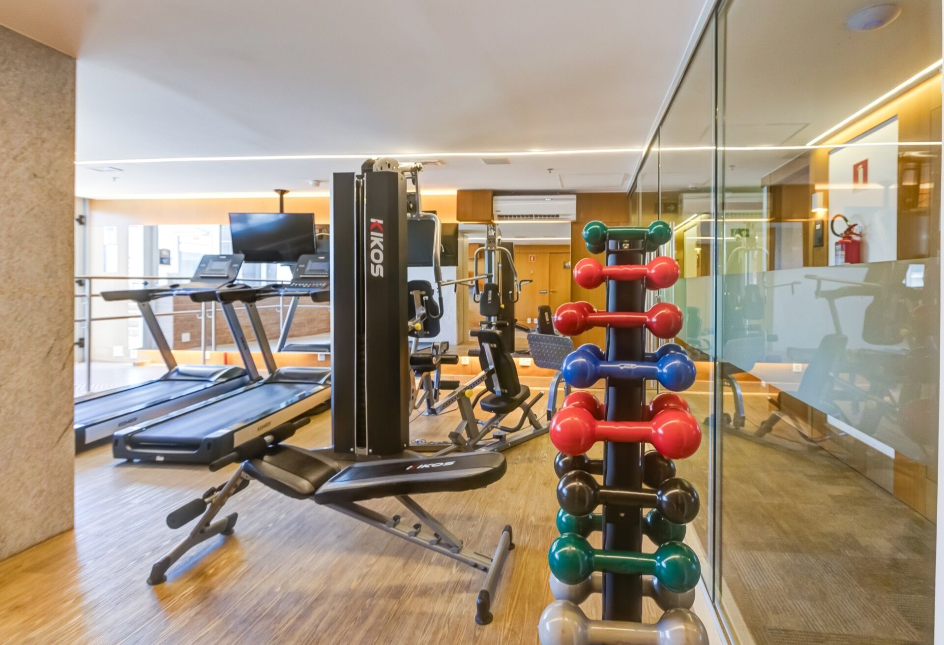 Un gimnasio con equipo de ejercicio, cinta de correr y pared espejada.