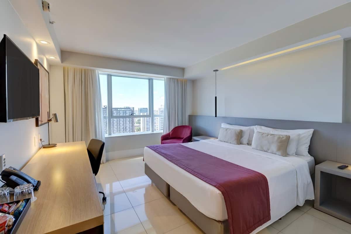 Habitación de hotel con cama, escritorio, silla, televisor y ventana con vista a la ciudad.
