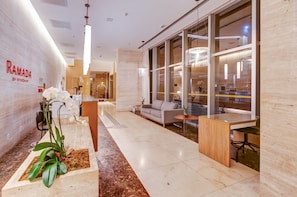 Un hall dâhĂŽtel moderne avec un comptoir dâaccueil, un espace salon et de grandes fenĂȘtres.