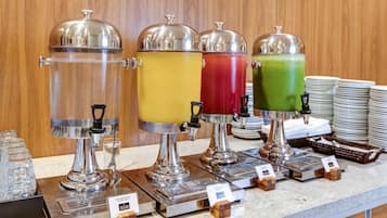 A beverage station with four dispensers, each with a different colored drink, and a stack of plates in the background.