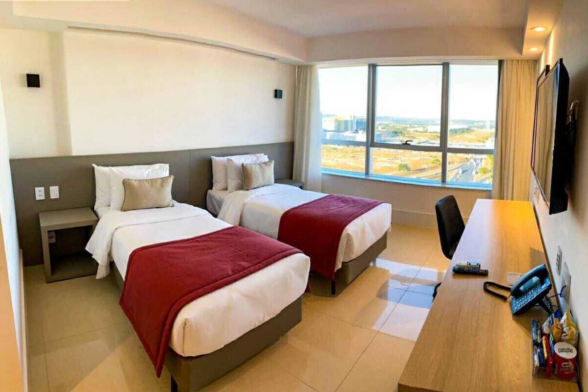 Habitación de hotel con dos camas, un escritorio, una silla, un televisor y una ventana con vista a la ciudad.
