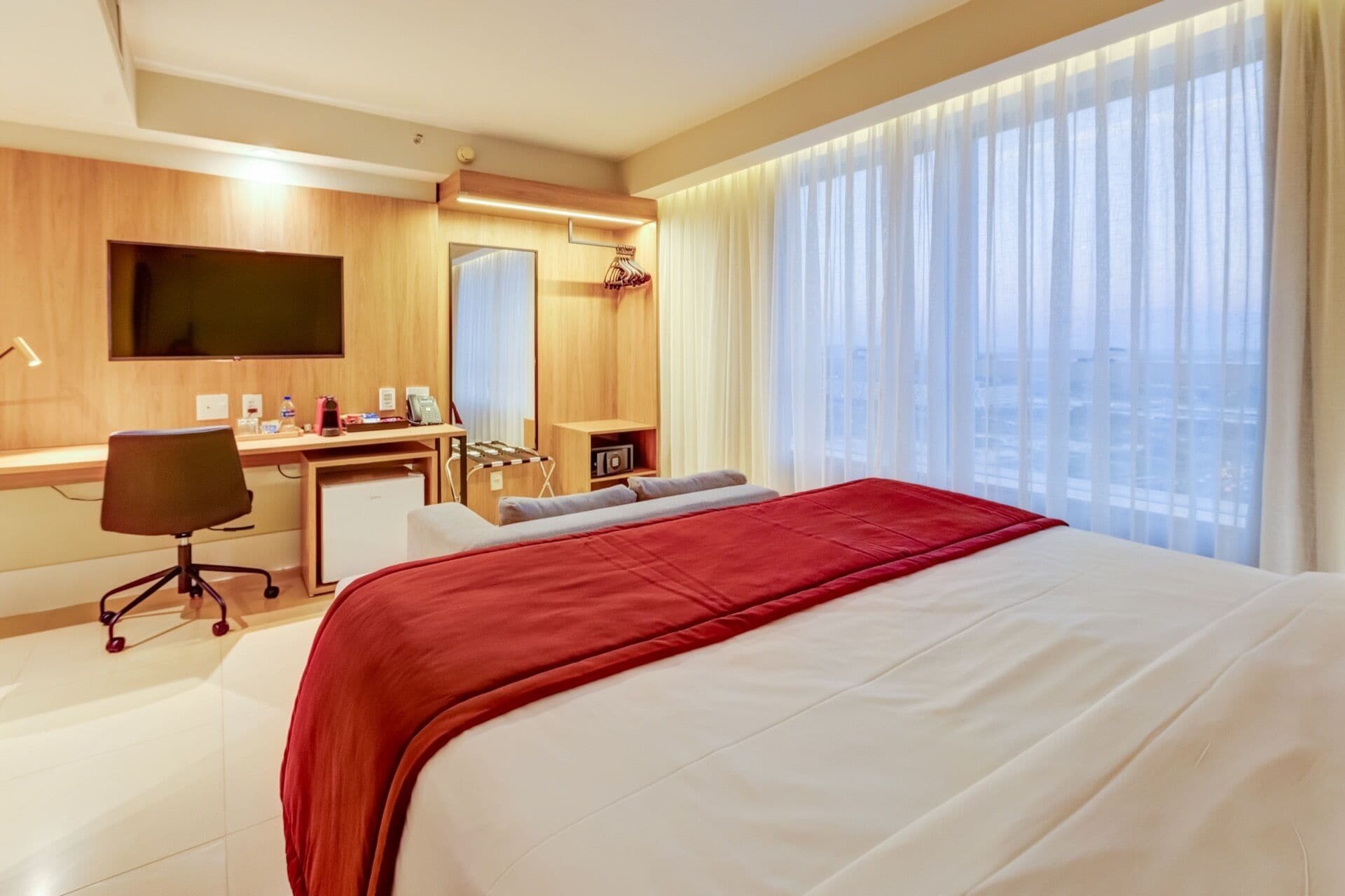 A hotel room with a bed, desk, chair, and a TV mounted on the wall.